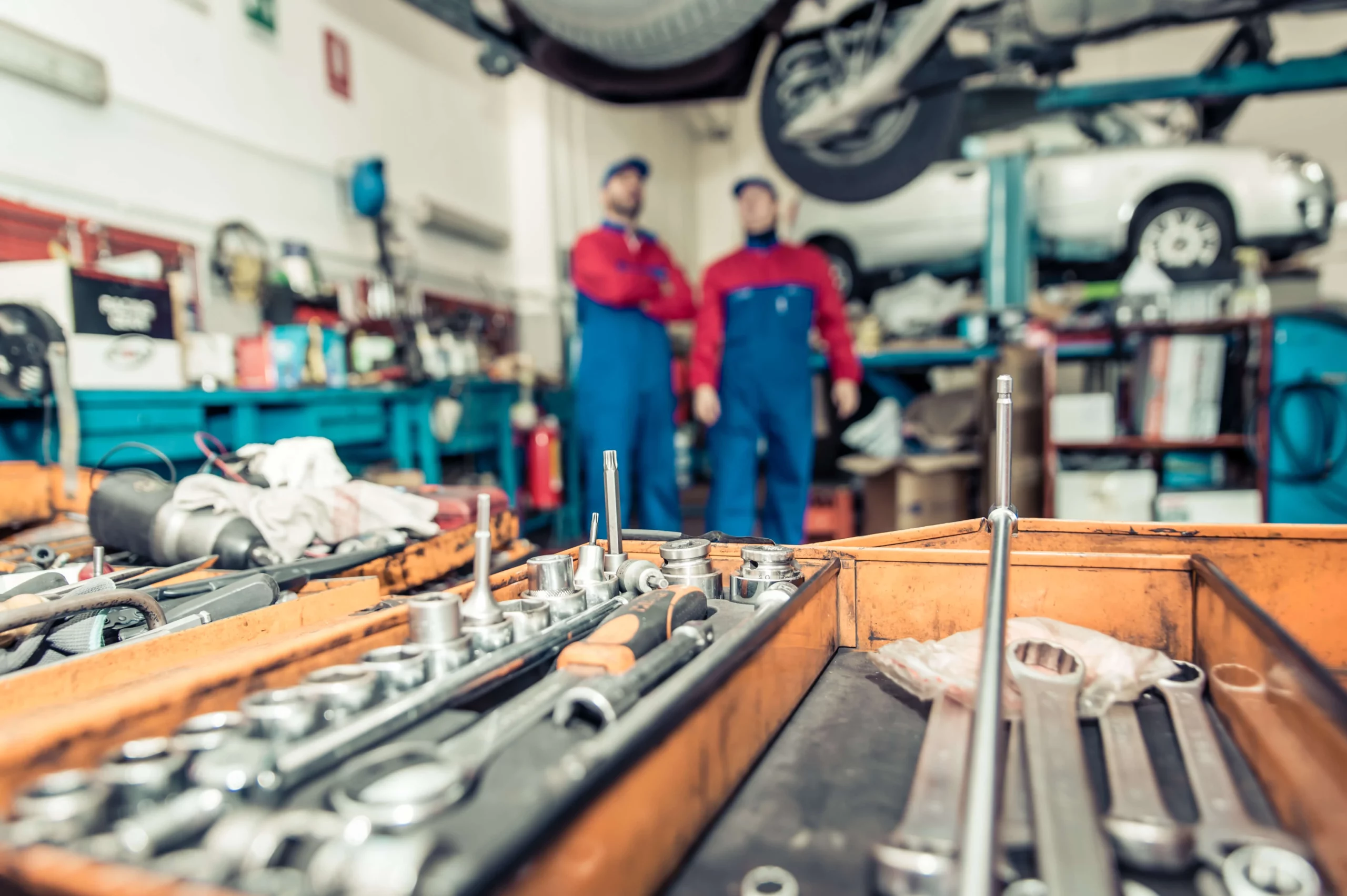 A well-equipped auto repair shop with an open toolbox in focus, while two mechanics stand near a lifted car, representing how much does it cost to open an auto repair shop with tools and labor.